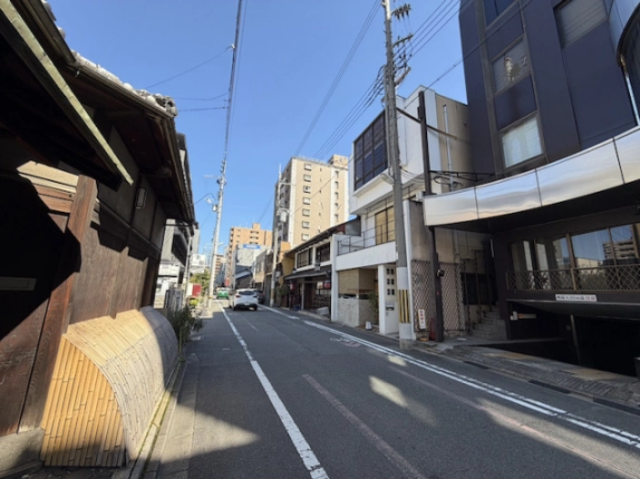 新町通を反対方向に見た様子。右手に◯△▢ビル、左手に町家の外壁と犬矢来