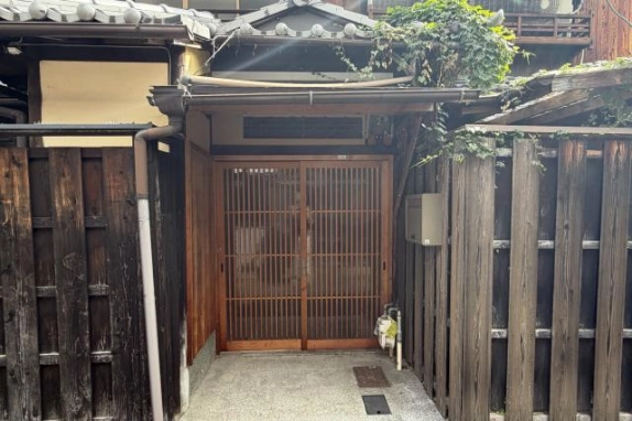 玄関の近景。2枚引きの木製格子戸の上に横長の明かり窓と瓦の小屋根があり、右側の板塀には蔦が絡む