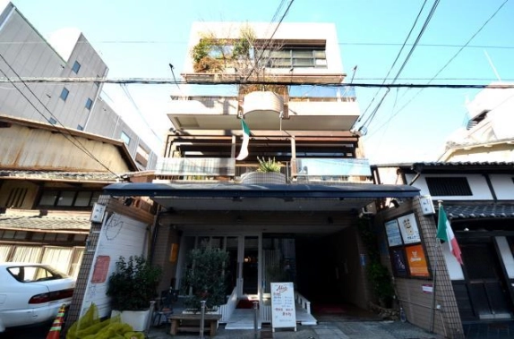 中京区の通りに面した4階建てビルを正面から見た外観。曲線のバルコニーや最上階の植栽があり、両隣に瓦屋根の建物が建つ