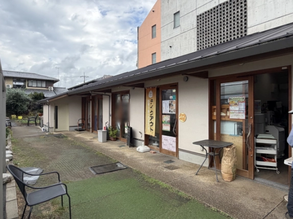 まえだ農園コミュニティーShopの通路側。人工芝と洗い出し舗装の通路に沿って、木枠のガラス引き戸が並ぶ平屋の店舗棟