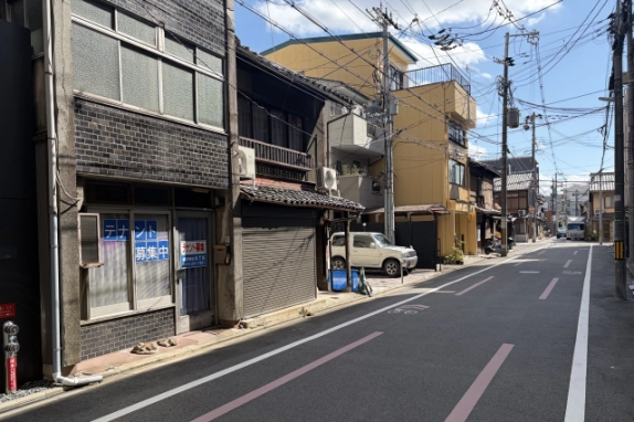 1階の窓と入口ドアを斜め前から見た様子。前面道路には自転車レーンの表示があり、奥へ電柱と家並みが続く