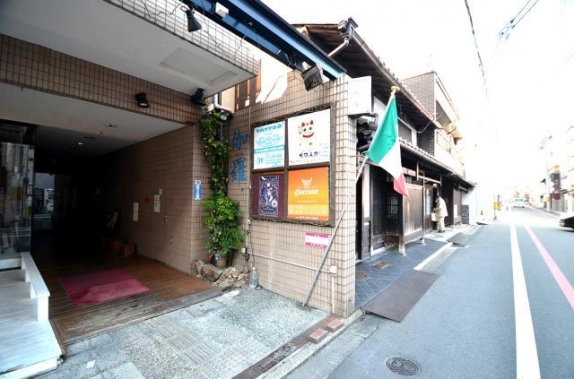 ビル1階の通路状のエントランスと、タイル壁に並ぶテナント看板。右隣には格子戸の町家が続く