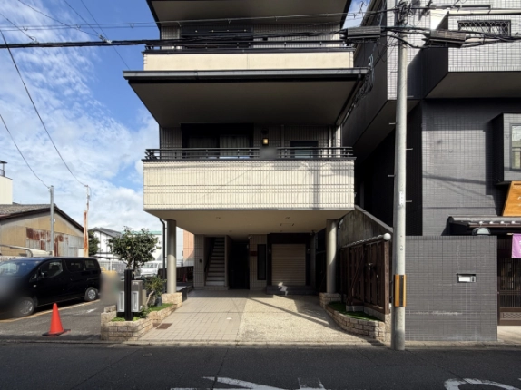 上珠数屋町店舗が入る3階建てビルを正面から見た外観。1階は2本の柱で支えたピロティで、奥に階段とシャッター