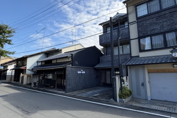 大徳寺向かいの紫野門前町の通り。瓦屋根の町家が並ぶ道路沿いに、前面空地のあるタイル張りの3階建てが建つ