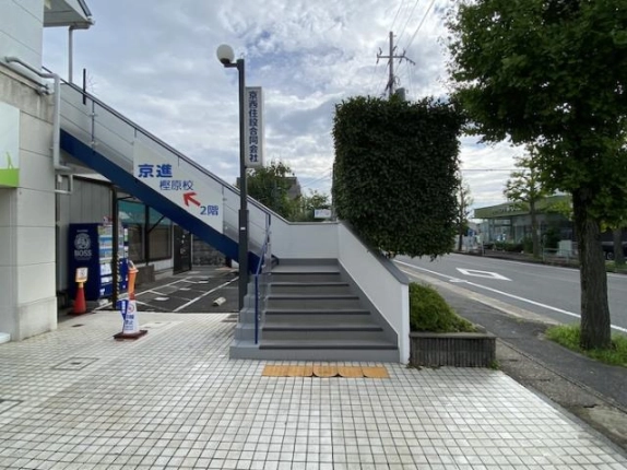 歩道から見た2階への外階段の上り口。青い手すりと灰色の段が続き、右側に山陰街道と街路樹