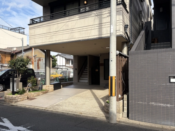 道路から見た1階ピロティ。左に植栽と郵便受け、中央奥に階段、右手前に電柱