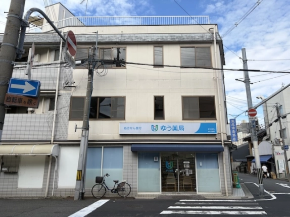 東山区弓矢町の3階建てビルを正面から見た外観。1階は紺色のテントがかかる薬局で、2階と3階に引き違い窓が並ぶ