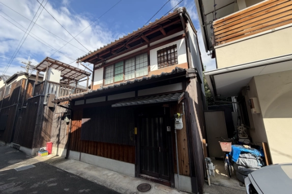 上京区石薬師町の京町家の外観。瓦屋根の木造2階建てで、1階に縦格子の窓と、小さな瓦の庇が付いた格子戸の玄関がある