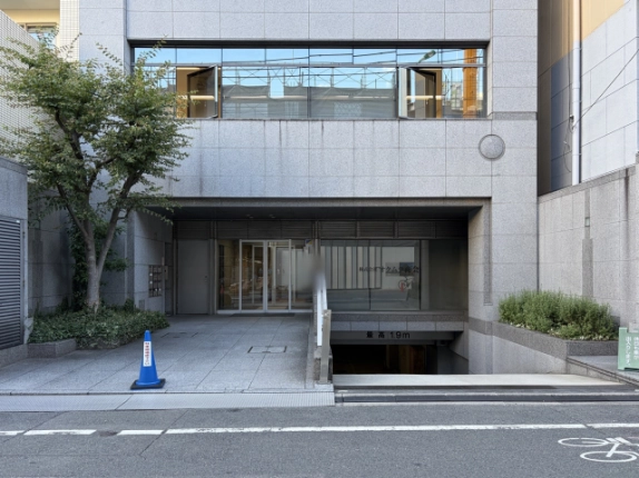 新町アイエスビルの正面外観。グレーの石張り外壁、植栽の奥にガラスの自動ドアのエントランス、右手に高さ制限1.9mの地下への車路