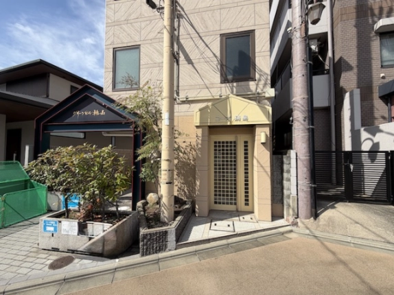 1階に店舗事務所区画があるコーポ鍋島の建物入口。淡い色の庇と格子状のガラス扉