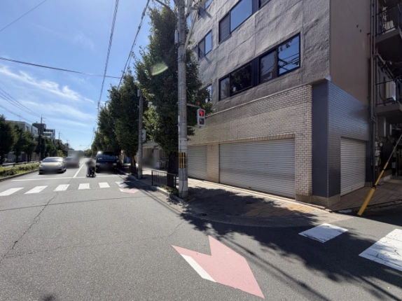 横断歩道の手前から見た1階の角部分。左にイチョウ並木の続く左京区の通り、右に白いタイル壁と下りたシャッター