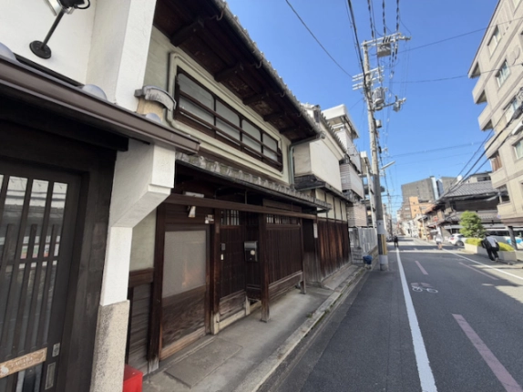 突抜町貸家の軒と入口まわり。木の格子戸の上に瓦のひさしと横長の窓がある