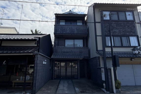 紫野門前町店舗事務所の正面外観。黒っぽいタイル張りの3階建てで、1階に瓦屋根の庇と格子入りのガラス扉、前面に石畳のアプローチがある