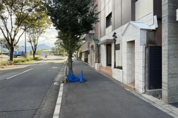 北山通に面した歩道と車道。右手に白いタイル張りの1階と黒い街灯、左手に植え込みと並木、奥に山並みが見える