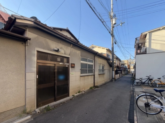 斜め前から見た瓦屋根の外観。玄関横に木製プレート、壁沿いに白い面格子付きの窓が2つ