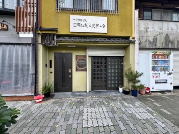 貸店舗事務所となる1階区画の正面。左に片開きの玄関ドア、中央に八角形の格子窓、右にシャッター付きの格子引き戸があり、上に瓦の小庇が付く