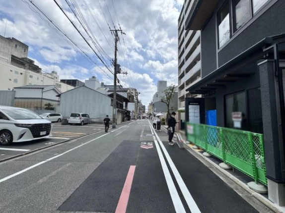 さきぞう室町会館前の道路。右手の建物と撮影時の緑色のフェンス、左手の駐車場