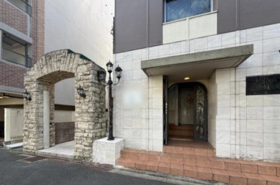 リバーコート北山の1階エントランス。グレーの庇の下に半円形のアーチ扉があり、手前にテラコッタ色のタイル階段、左隣に石積みのアーチと黒い街灯が立つ