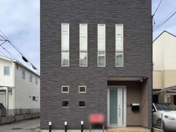 西京区川島滑樋町の一棟建物を正面から見た外観。濃いグレーのタイル外壁に縦長の窓が4列並び、右側の庇の下に白いガラス入りの玄関ドアとポストがある