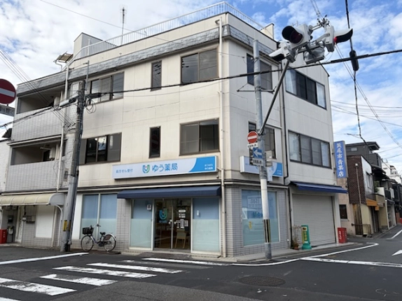 松原通と大和大路通の北東角地に建つビルを、交差点の斜め向かいから見た外観。角をはさむ2面の外壁と1階の薬局が見える