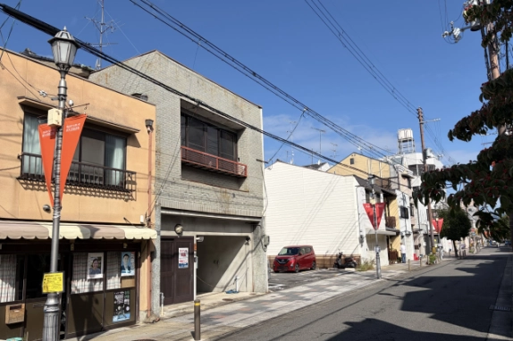 北大路駅から徒歩17分の通り沿いに建つ外観を、街灯のある歩道側から見た様子。右手に駐車場と奥へ延びる道路