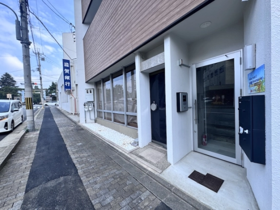 上階へ続く階段が見えるガラス扉。西工務店ビル入口のインターホンと郵便受け