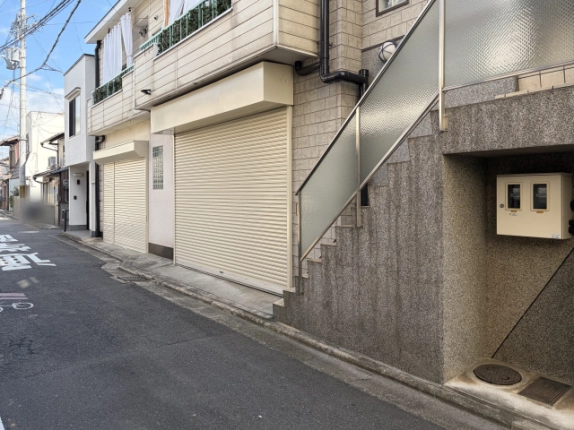 右斜め前から見た1階のシャッター。手前に曇りガラスの手すりが付いた石目調の外階段、階段下にメーターボックスがある