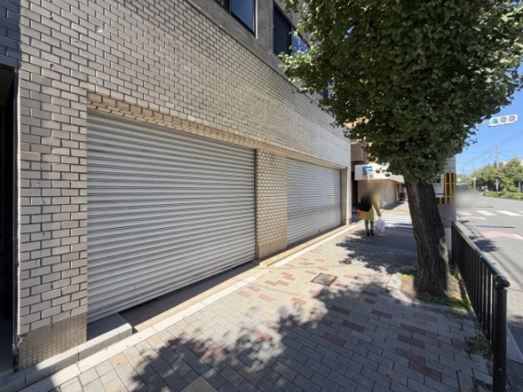 斜めから見た1階の2枚のシャッター。右手の歩道にイチョウの木と柵が続く