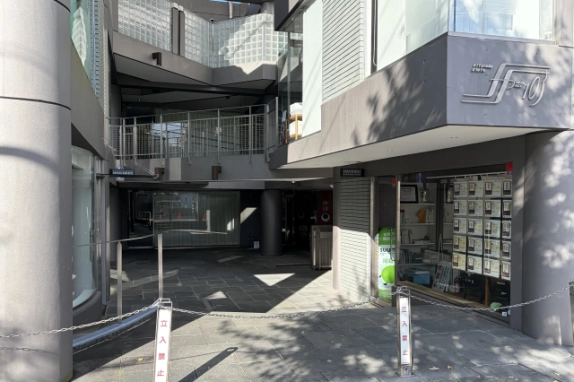 建物中央の通り抜けエントランス。石張りの通路の奥に吹き抜けと上階の手すり付き廊下が見え、右手に「103」のロゴ看板と1階店舗のガラス窓、手前に立入禁止のチェーンが張られている