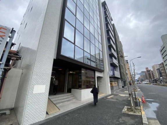 烏丸通の歩道から見た低層部。街路樹が並ぶ歩道に面して、階段とスロープを備えた入口がある