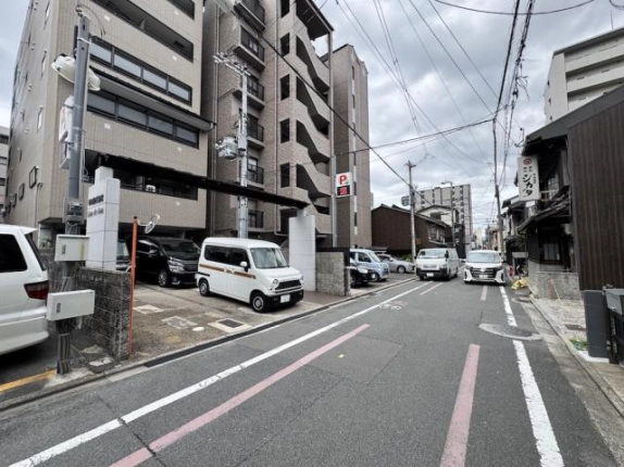 建物を左手に見た前面道路。右側に木造の町家が並び、通りの奥に白い車が見える