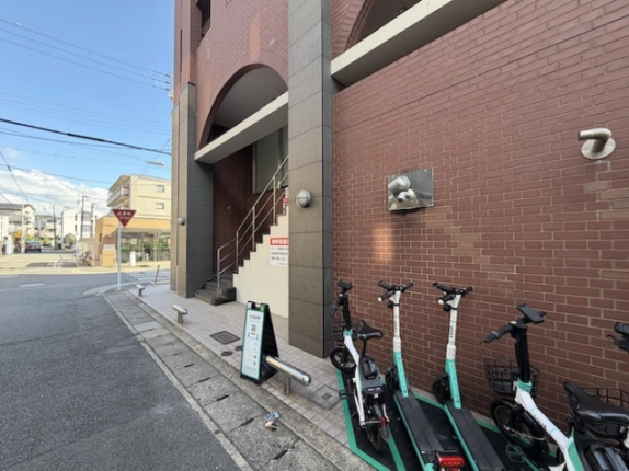 2階へ上がる階段を反対側から見た様子。赤茶色の外壁と手前に並ぶシェアモビリティ