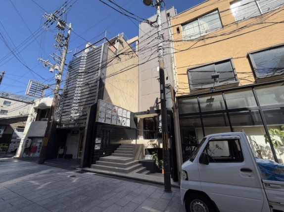 東山区祇園の石畳の通りを左斜めから見たビルと周辺。電柱と電線が並び、右隣の建物の前に白い軽トラックが停まっている