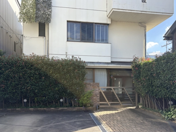 出水町店舗事務所の1階入口付近。ガラス扉とカーテンの掛かった窓、レンガの門柱と斜め格子の門扉、生垣の足元に庭園灯が並ぶ