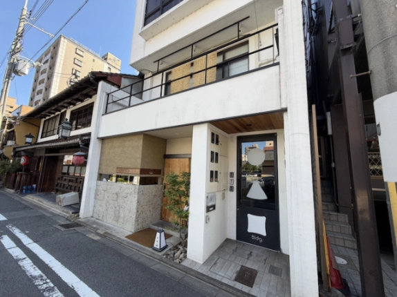 2階に貸事務所がある◯△▢ビルの低層部。黒い手すりと道路に面した入口