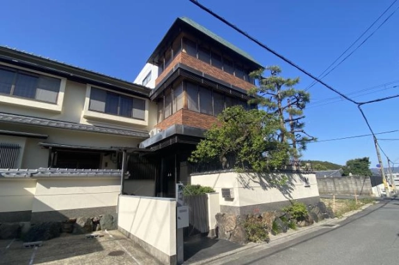 道路から斜めに見た一括貸店舗事務所の外観。左に瓦の庇があるクリーム色の2階建、右にレンガ調の3階建が並び、間に門のある入口