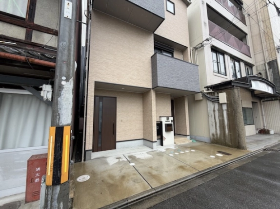 道路側から見た建物低層部。入口前のコンクリート舗装と丸い排水ます