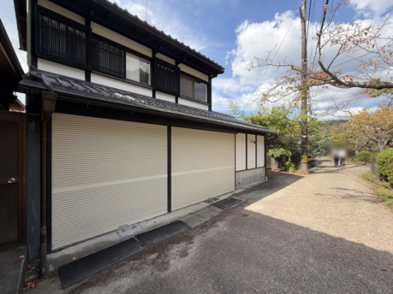 右斜めから見た店舗の外観と、右側に続く桜並木の砂利道