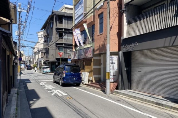 SAKURA BLD.祇園前の道路。右手に建物入口と店舗看板、奥に交差点