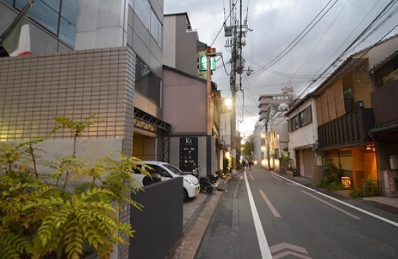建物前から奥へ続く通りの様子。左手にタイル張りの壁と植栽、右手に格子のある建物