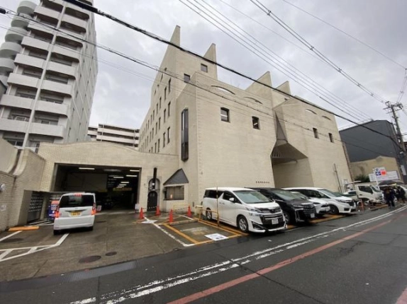 右斜め前から見た外観。左手に屋内駐車場の出入口、縦長の細い窓、小さなアーチ形の扉があり、建物前に駐車区画がある