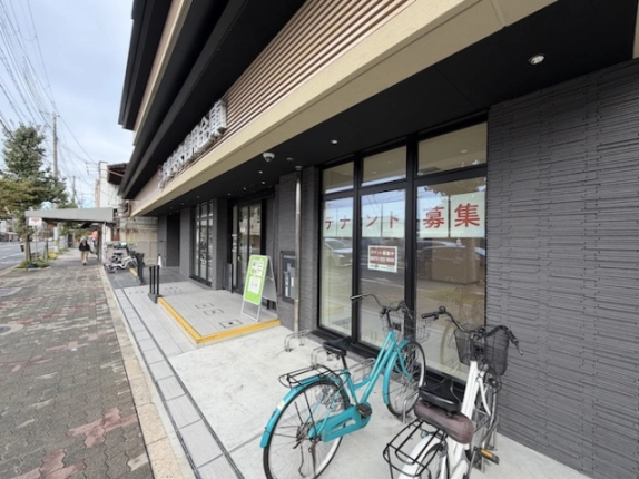 1階貸店舗の募集案内が貼られたガラス面。入口前の手すりと段差、手前の自転車