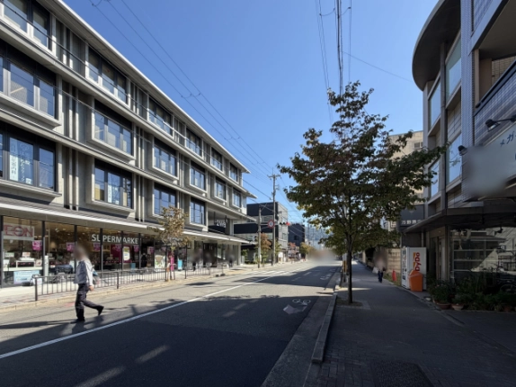 2waが面する左京区の通りを反対方向から見た街並み。左に1階スーパーマーケットの店先、道路を挟んだ右側には街路樹と自動販売機のある歩道が続く