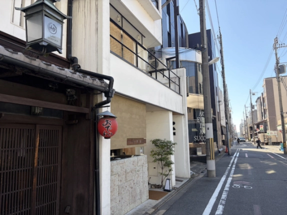 ビルを左手に見た新町通。隣接する町家の格子戸と奥へ続く前面道路