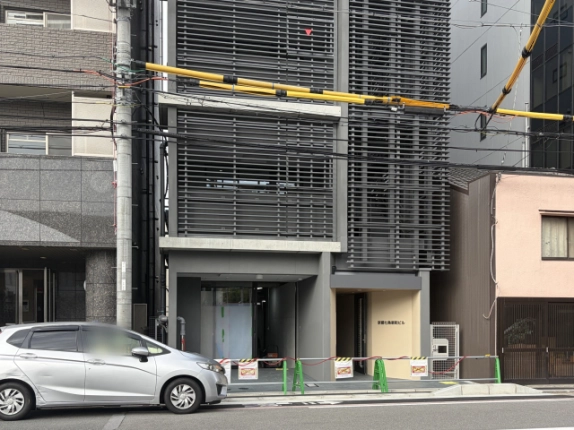 京都七条新町ビルの正面外観。グレーの横ルーバーで覆われた建物の1階に、左側のガラス面の区画と右側のベージュ壁のエントランスが並ぶ