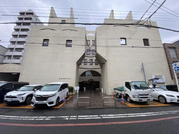 中京区玉蔵町の美濃利ビルを正面から見た外観。左右対称の白い外壁の中央にアーチ形の開口と網目状の庇がある通路型の入口があり、入口前に車止めの柵が立つ