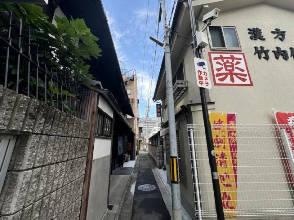 七条西洞院周辺の路地入口。左手の塀と植栽、右手の薬店の間を通る細い道