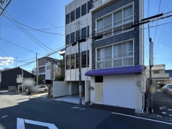 大宮三条テナントビル（左の白い建物）を斜め前から見た外観。右隣は紫色の庇とシャッターのある紺色タイル張りの建物