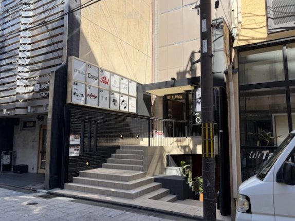第二EFビルの入口まわり。各階のテナント看板が並ぶ黒い壁の横に、手すり付きの階段と「EF II Bldg.」の表示がある入口が見える