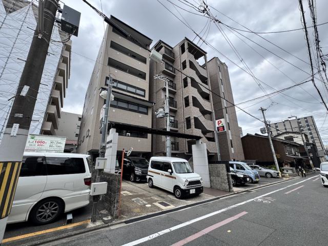 下京区喜吉町のCasa de issaを斜め前から見上げた外観。ベージュの外壁に横長の窓が並び、右隣に茶色いタイル張りのマンションが建つ